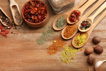 Assorted spices in spoons on wooden table, top view