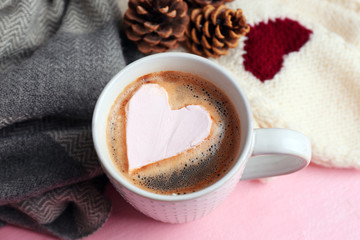Cup of hot cappuccino with heart marshmallow and warm clothes on pink background, close up