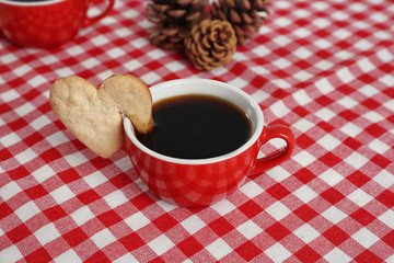 Heart shape cookie on cup of coffee on checkered napkin closeup