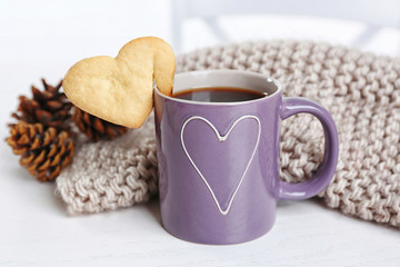 Heart shape cookie on cup of coffee with knitted cloth closeup