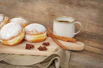 Delicious sugary donuts with spices and cup of coffee on wooden background
