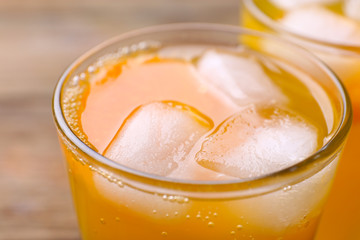 Glasses of orange juice with ice block on wooden background, close up