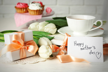 Happy mother day greeting with tulips, cup of tea and delicious cupcakes on wooden table closeup