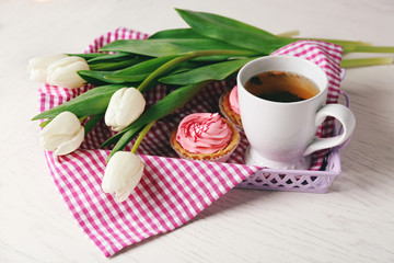 Still life with fresh bouquet of tulips, cupcakes and cup of tea on wooden table closeup