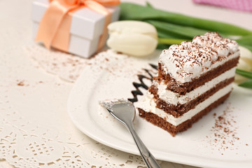 Sweet creamy cake with flowers and present box on wooden table closeup