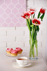 Still life with cup of tea, cupcakes and bouquet of tulips on brick wall background