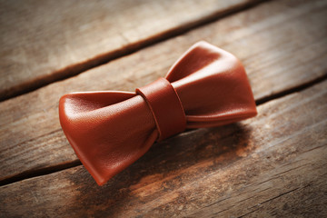 Light-brown leather bow tie on a brown wooden background
