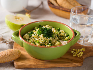 Millet porridge with broccoli in a green bowl on beige table cloth