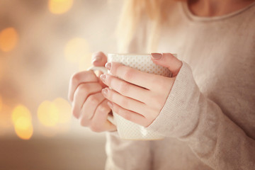 Woman in a white knitted sweater holding a cup of tea in her hands, close up