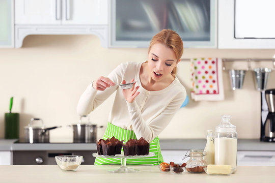 Young woman decorating fresh baked cupcakes with a sugar powder