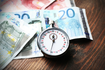 Stopwatch with euro banknotes on wooden background. Time is money concept