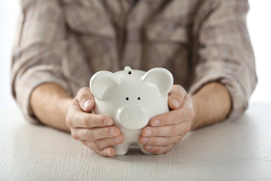 Male hands holding piggy bank at wooden table closeup