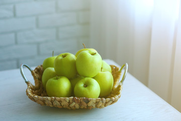 Ripe green apples in a wicker basket on a kitchen table