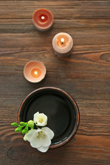 Beautiful flower in the bowl with water and candles on wooden background