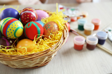 Fototapeta na wymiar Colorful Easter eggs in wicker basket with paint on wooden table closeup