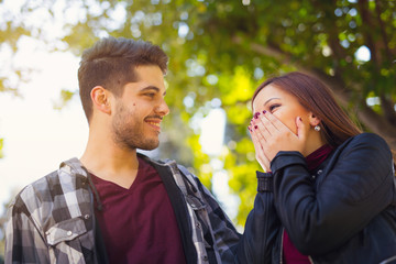 Fototapeta premium Young couple in the park. Girl holds hand on her mouth. Selective focus