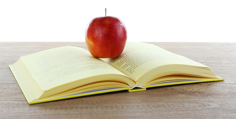 Open book with red apple on table