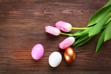 Three Easter eggs with pink tulips on wooden background