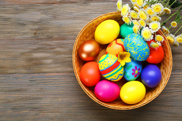 Easter eggs in basket with spring flowers on wooden background