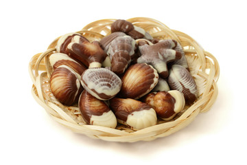 chocolate candy shaped sea shells in a wicker basket on the white background