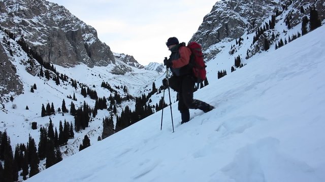 Tourist with a backpack walking on snow-covered mountain path on the background of an evening mountain landscape