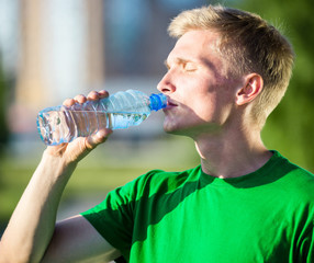 Tired man drinking water from a plastic bottle after fitness