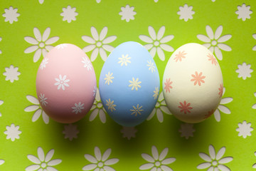 Three Easter eggs in pastel color on patterned background