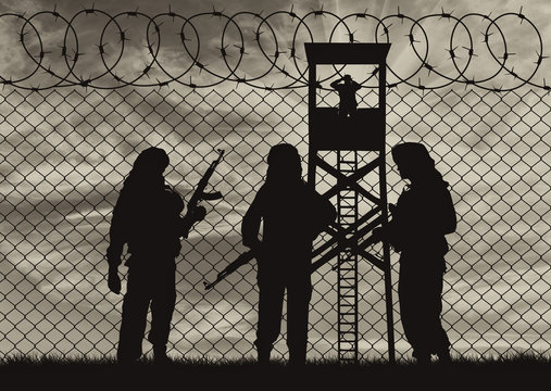 Silhouette of men with rifle standing near border fence