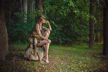 Fototapeta premium Elegancka piękna młoda Amazonka długowłosa i długonoga siedząca na skale w lesie
