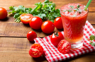 Gass of tomato smoothie, fresh tomatoes and cilantro on a dark wooden background . Vegetarian or healthy eating concept