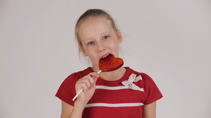 Young girl sitting on the swing and enjoy candy.Young girl sit on a swing and eat lollipop.Adorable little girl with red lollipop in heart shape isolated over white background.