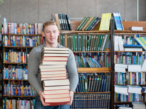 Portrait of a male student with pile books in college library