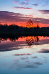 Fototapeta na wymiar Beautiful sunset over the lake with colorful red sky and reflections in calm water