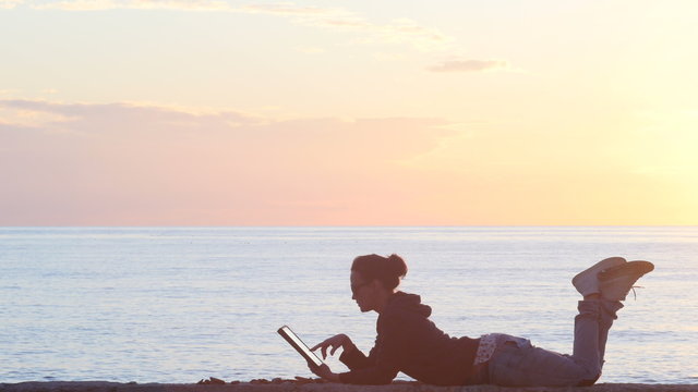 Woman using a tablet on the beach during sunset