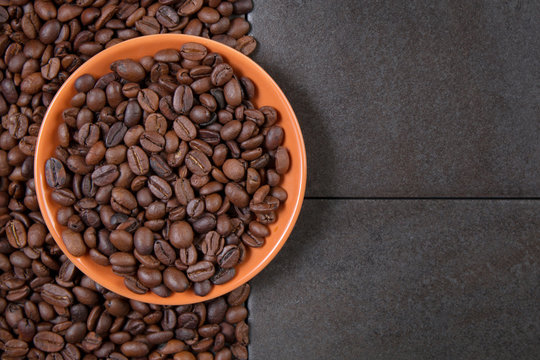 coffee beans in an orange plate on a dark stone background