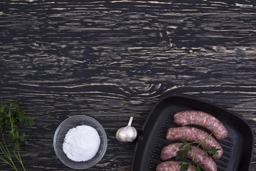 raw sausage in  frying pan with garlic on wooden background