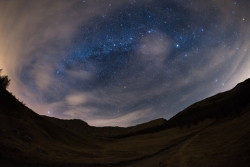 180 degree view of the starry sky and Milky Way on the Alps with blurred motion clouds drawing...