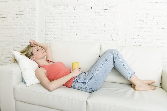 young attractive blond hair woman holding cup of coffee lying on sofa couch at home living room sleeping relaxed
