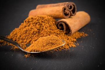 cinnamon sticks with powder on dark stone plate