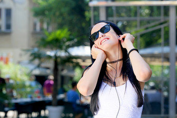 beautiful young black hair woman with sunglasses listening music with earphones in the city