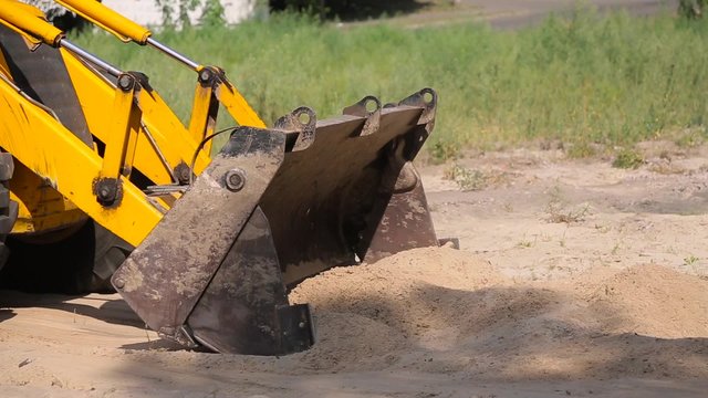 Yellow bulldozer rows sand in the bucket.