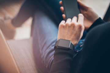 Fototapeta premium Closeup photo of female hands touching screen smartphone and wearing generic design smart watch. Film effects, blurred background. Horizontal