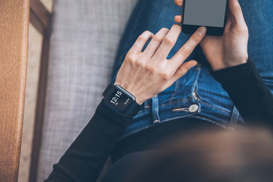 Photo of female hands touching screen smartphone and wearing generic design smart watch. Film effects, blurred background. Horizontal