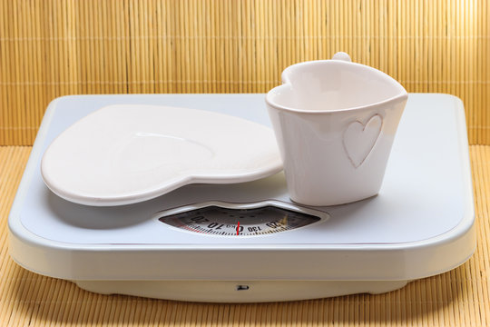 Empty plate saucer and mug cup on weighing scale.