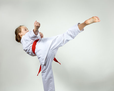 Young girl in a kimono with a red belt makes kicking karate