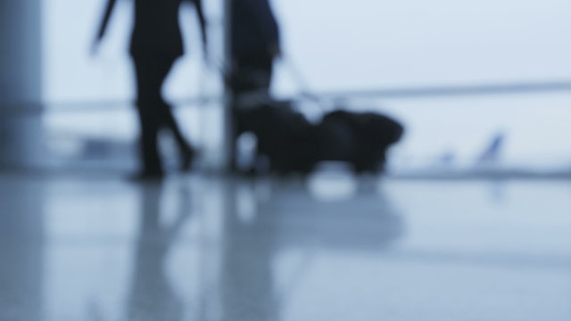 Airport terminal. People walking out of focus and blurry with luggage. Low section of passengers are walking fast by window. Traveling and Air travel concept.