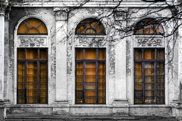 Fototapeta na wymiar Facade of old abandoned building with three large arched windows of orange glass. Monochrome background