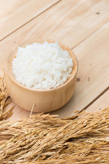 bowl full of rice and ear of rice on wooden background