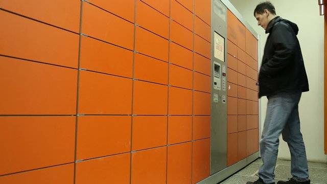 A man receives a package in the mail postal terminal, he enters the mailing code on the touch screen of terminal
