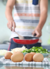 Lunch time! Man holding pan in the kitchen, eggs in the foreground
